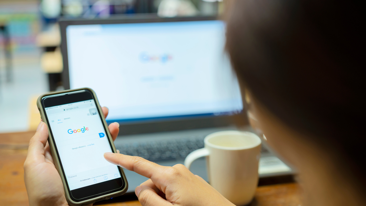 Student som tittar på Google på sin mobiltelefon och i bakgrunden kan vi se en bärbar datorskärm också med Google.