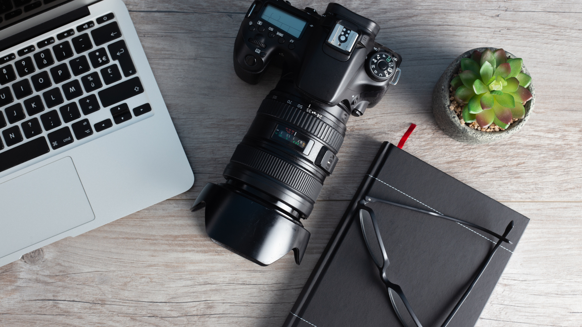 DSLR-kamera på ett bord med ett anteckningsblock och en bärbar dator.